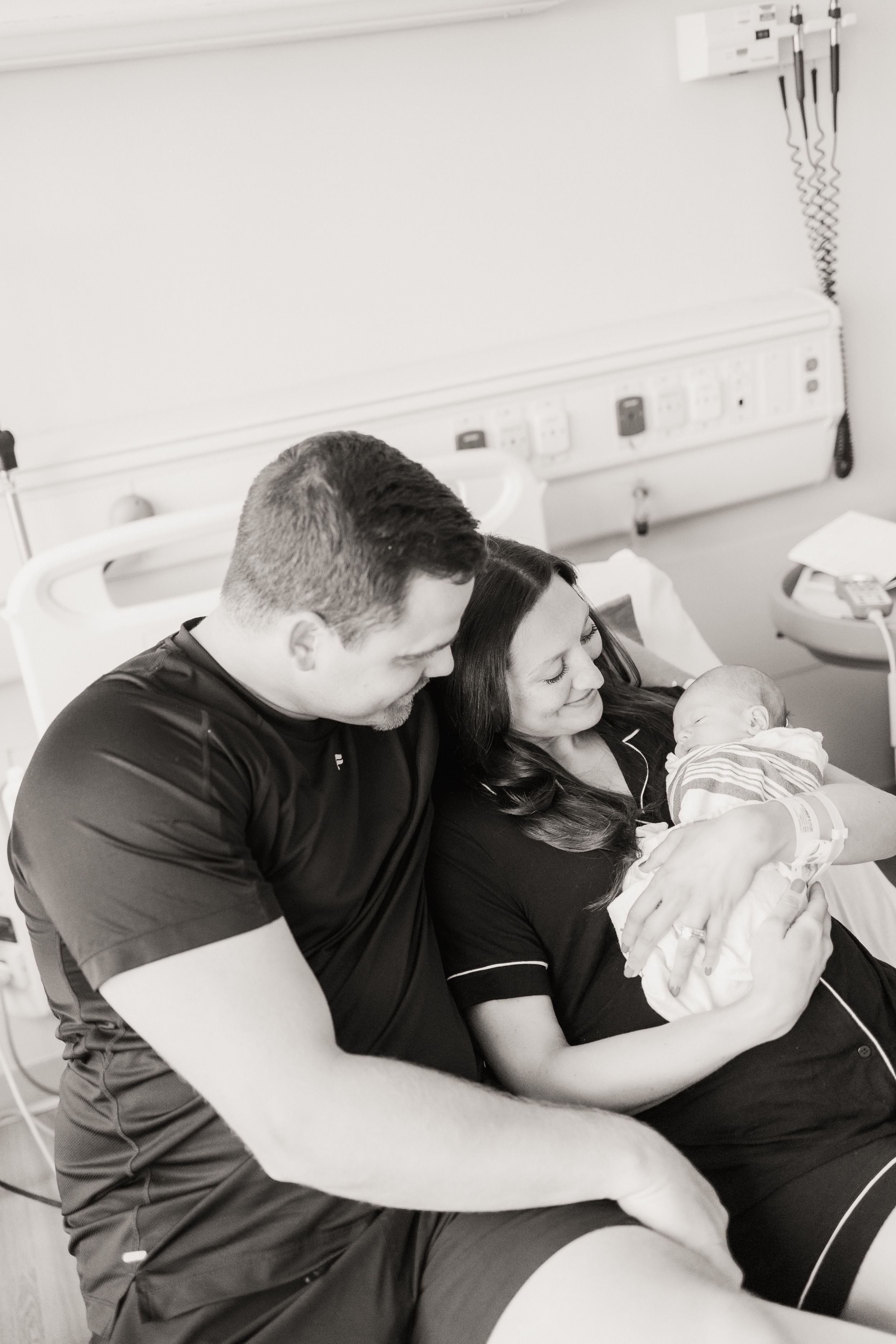 Black and white photo of parents with newborn baby in hospital room.