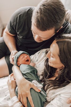Parents lovingly gaze at their sleeping newborn baby swaddled in a green blanket in a series of intimate photos.