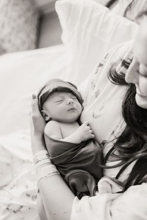 Black and white photo of sleeping newborn nestled against soft bedding.