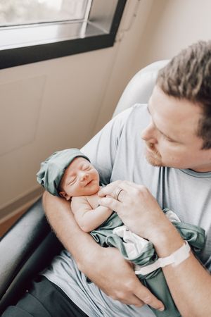 A sleeping newborn baby swaddled in a teal blanket being held in someone's arms.
