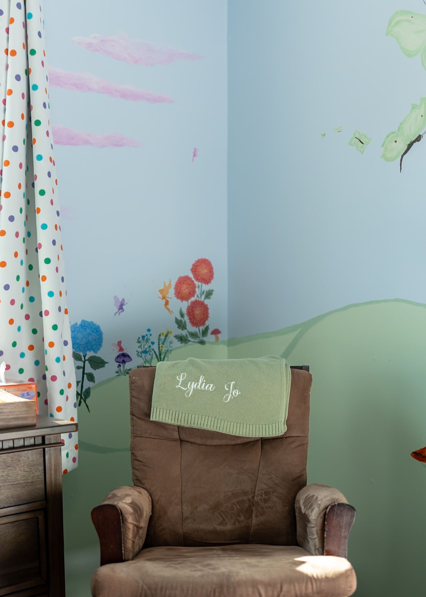 Nursery room with floral wall decals and brown armchair with personalized blanket.