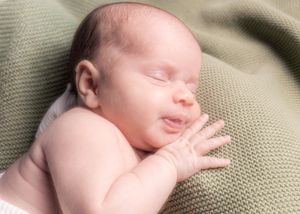 Peaceful sleeping newborn on textured sage green blanket.