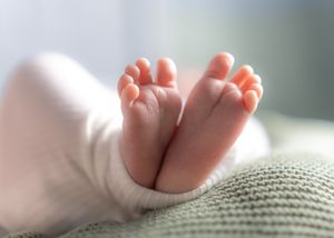 Close up of tiny newborn baby feet against soft gray fabric.