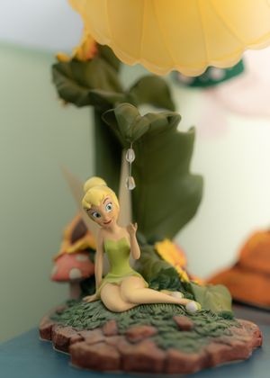 Tinker Bell figurine sitting on decorative base with leaves and yellow details.