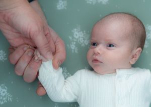 Gentle hands adjusting white wrap on resting baby against mint floral background.