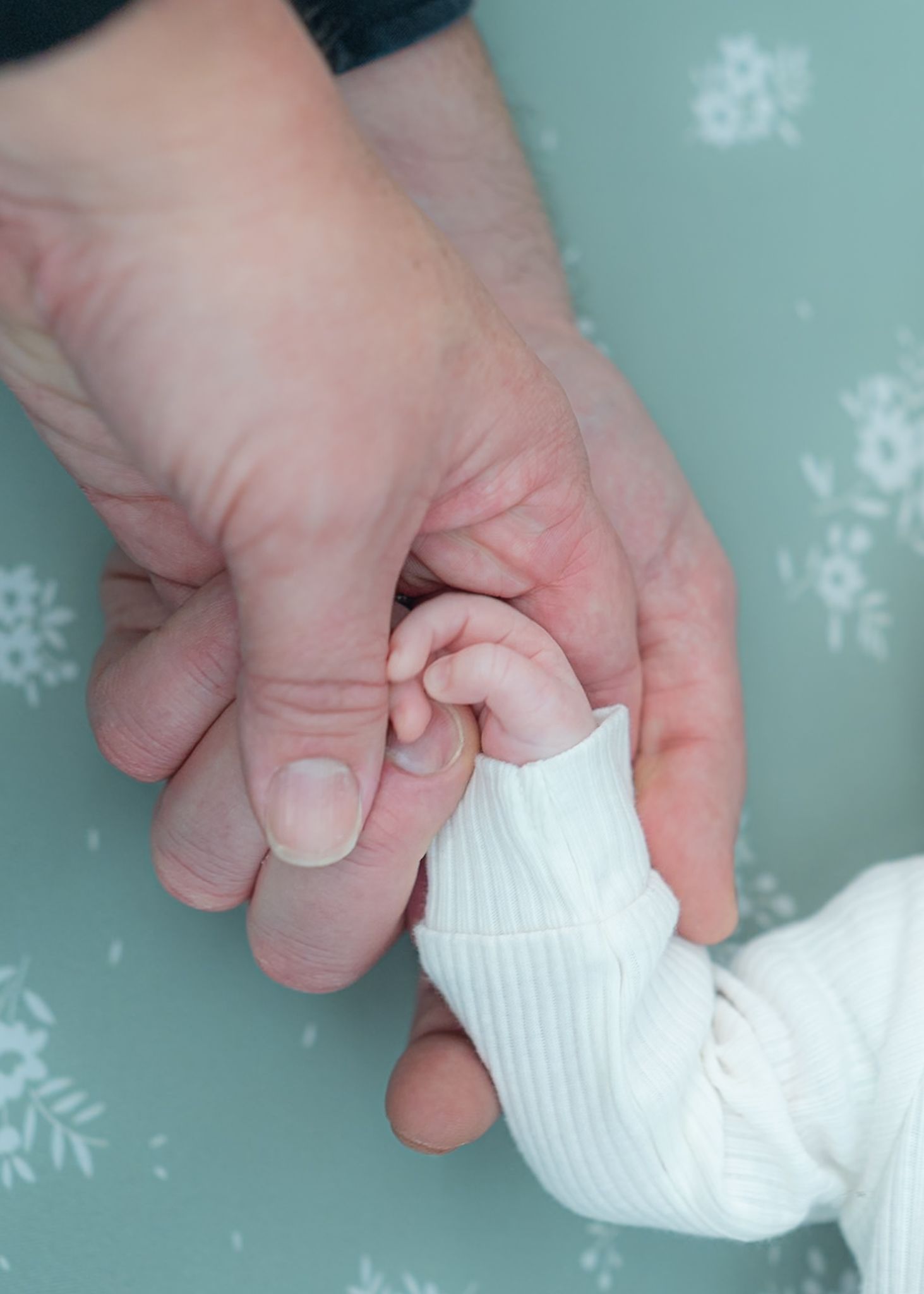 Hands carefully wrapping white fabric around newborn during photo session.