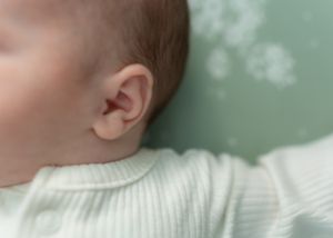 Newborn baby wrapped in white fabric against a mint green background.
