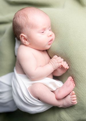 Sleeping infant in white clothing resting on sage green textured fabric.