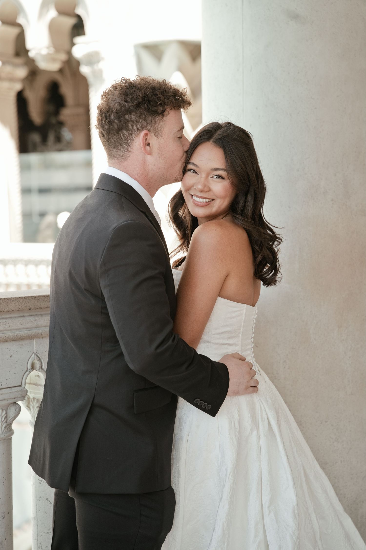 Newlyweds sharing a kiss at the altar during outdoor wedding ceremony with white chairs and trees.