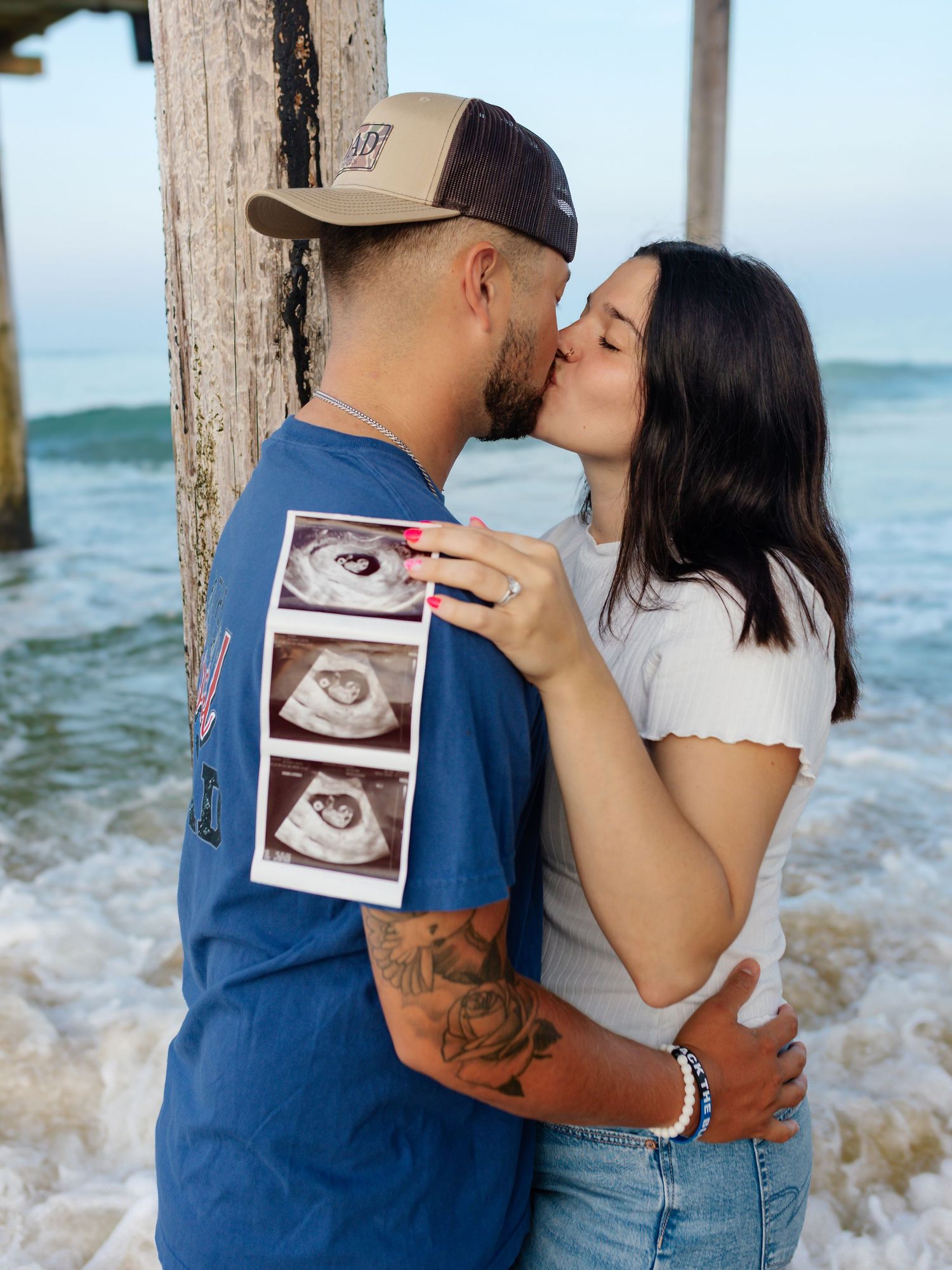 Couple sharing romantic moment by pier while holding ultrasound photos.