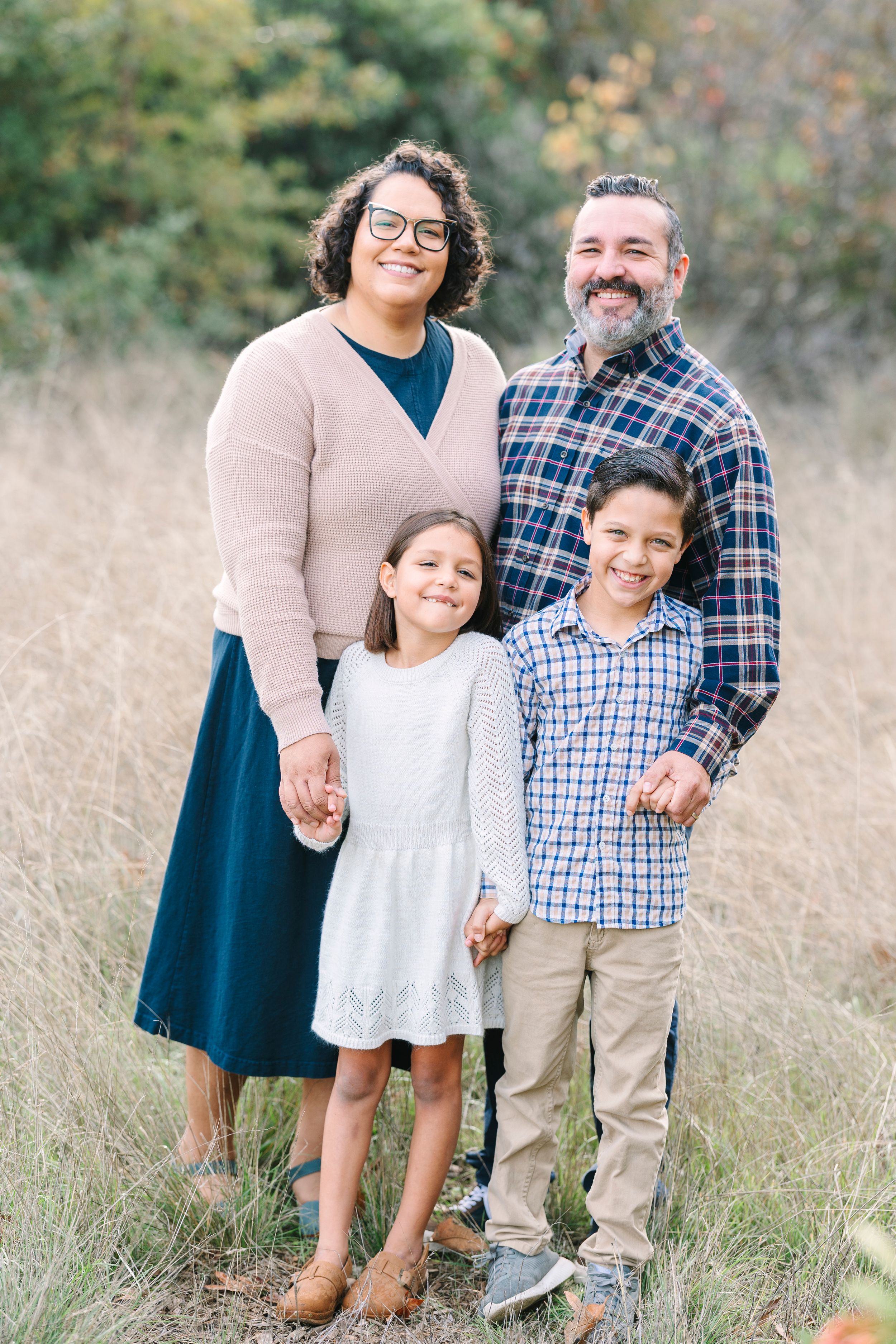 Family portrait in casual attire standing together in a tall grass field.