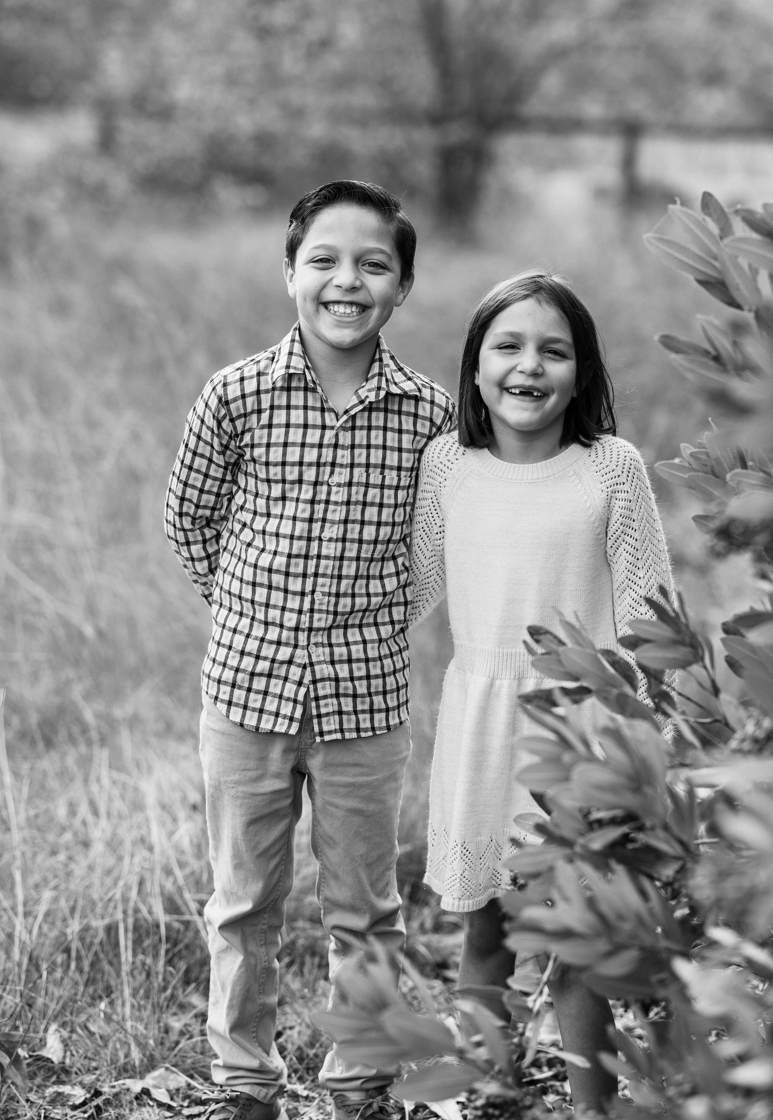 Black and white photo of two children laughing together by foliage.
