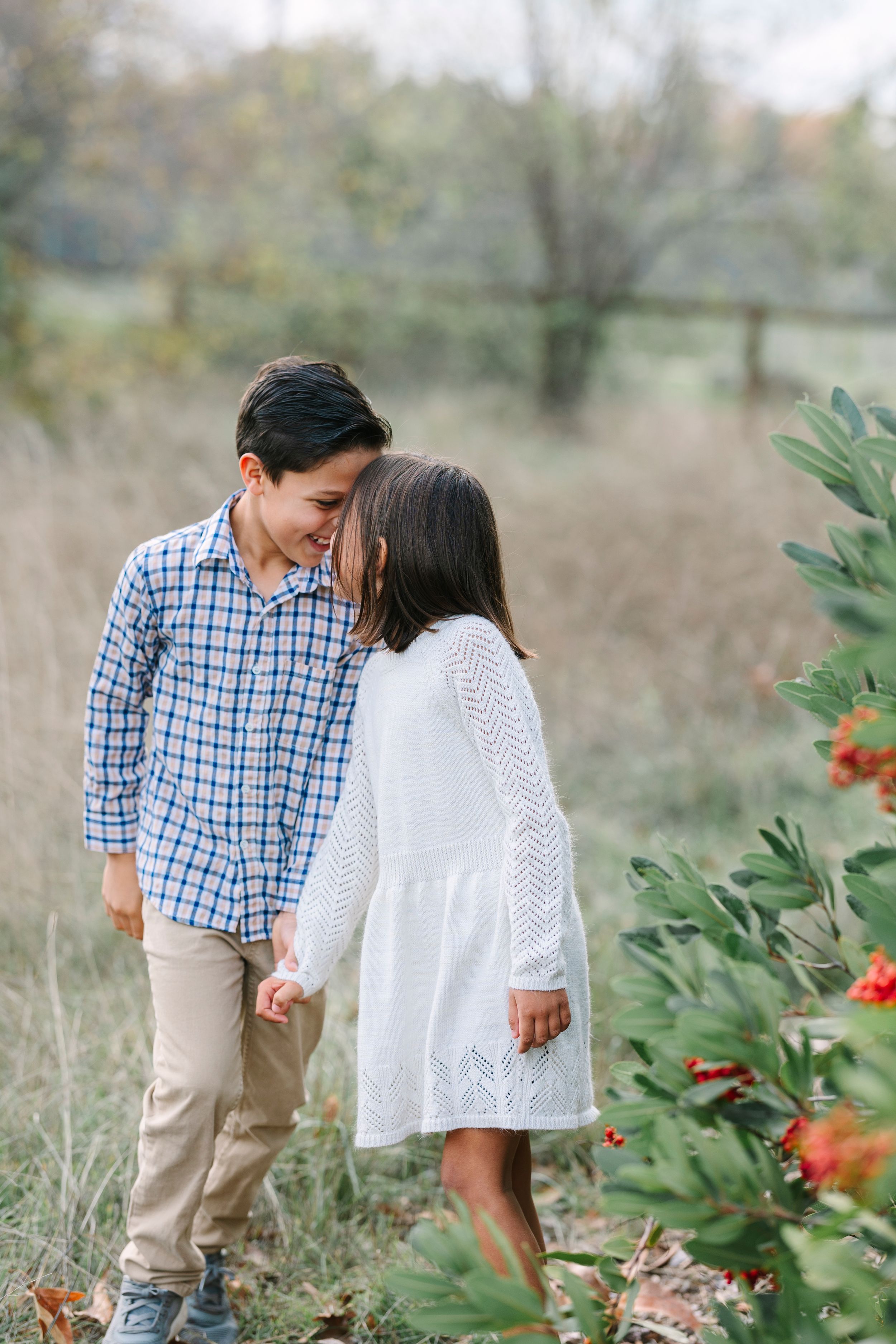 Children in casual attire playing near flowering bushes in a natural setting.