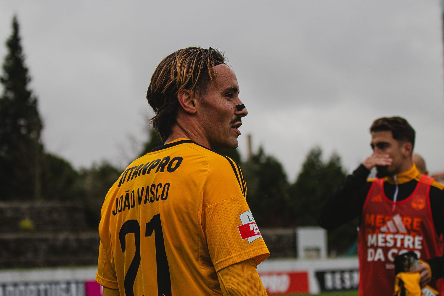Soccer match between teams in yellow and white uniforms under overcast skies.
