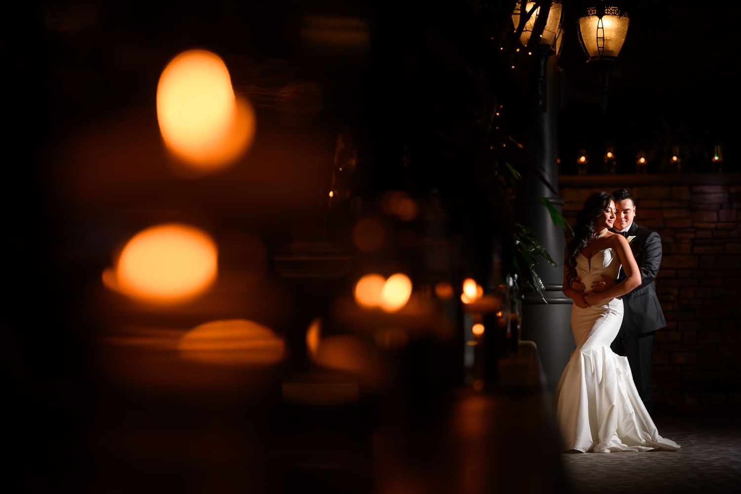 Romantic wedding couple dances under warm glowing lanterns in a dimly lit venue creating an intimate atmosphere.
