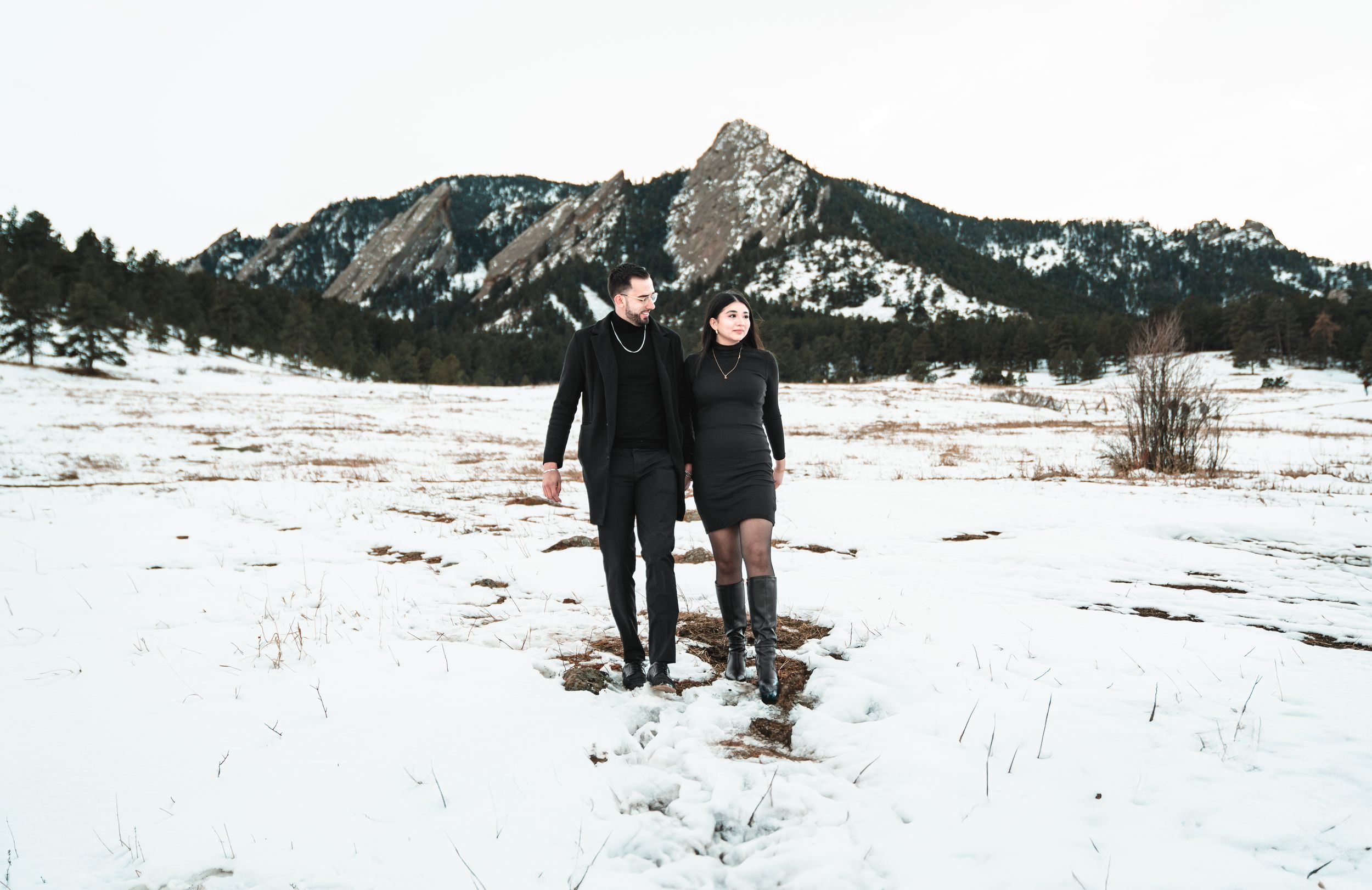 People walking through a snowy mountain landscape with dramatic winter peaks and white terrain stretching into the distance.