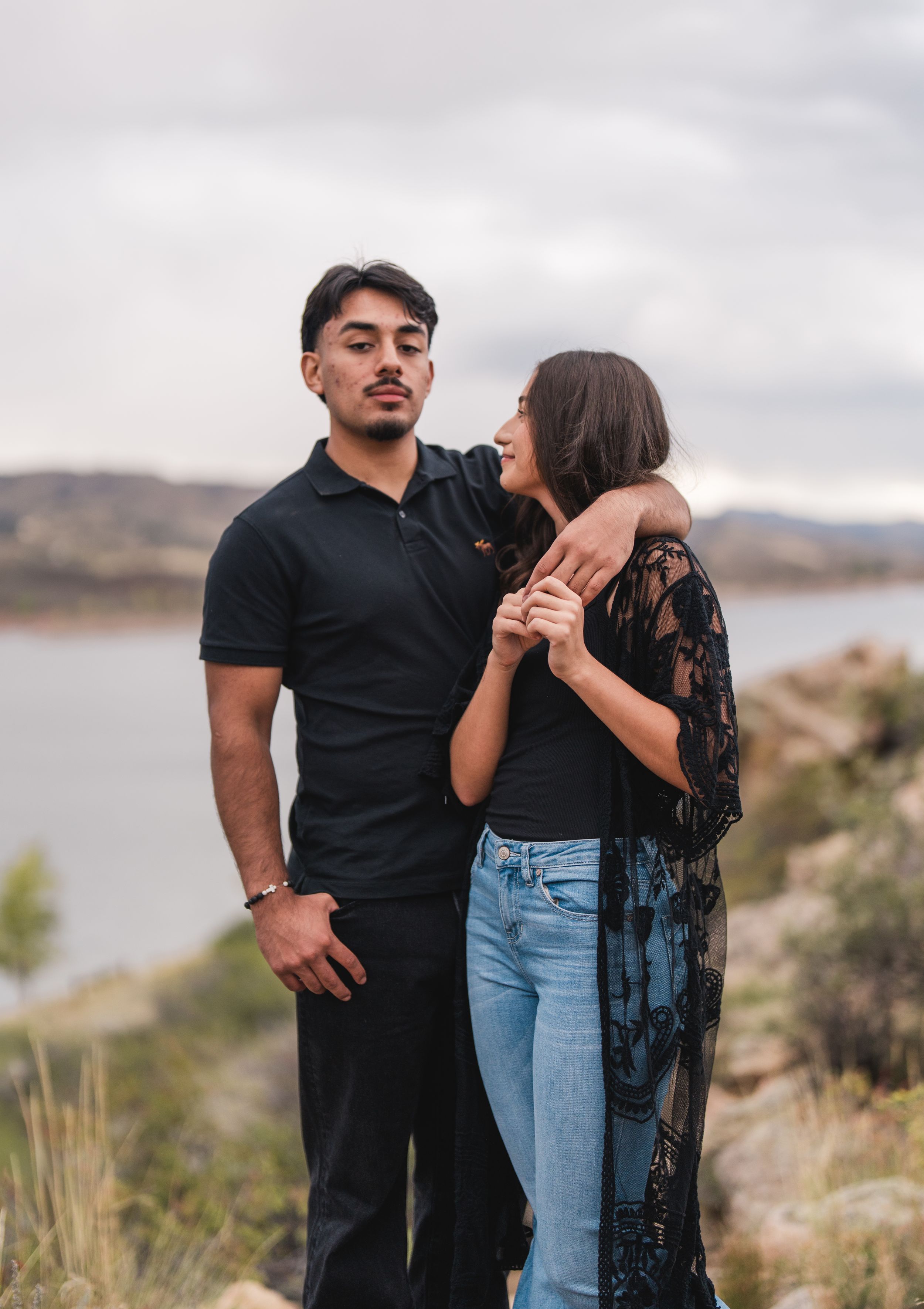 A couple embraces against a scenic desert landscape with mountains and a lake in the background.