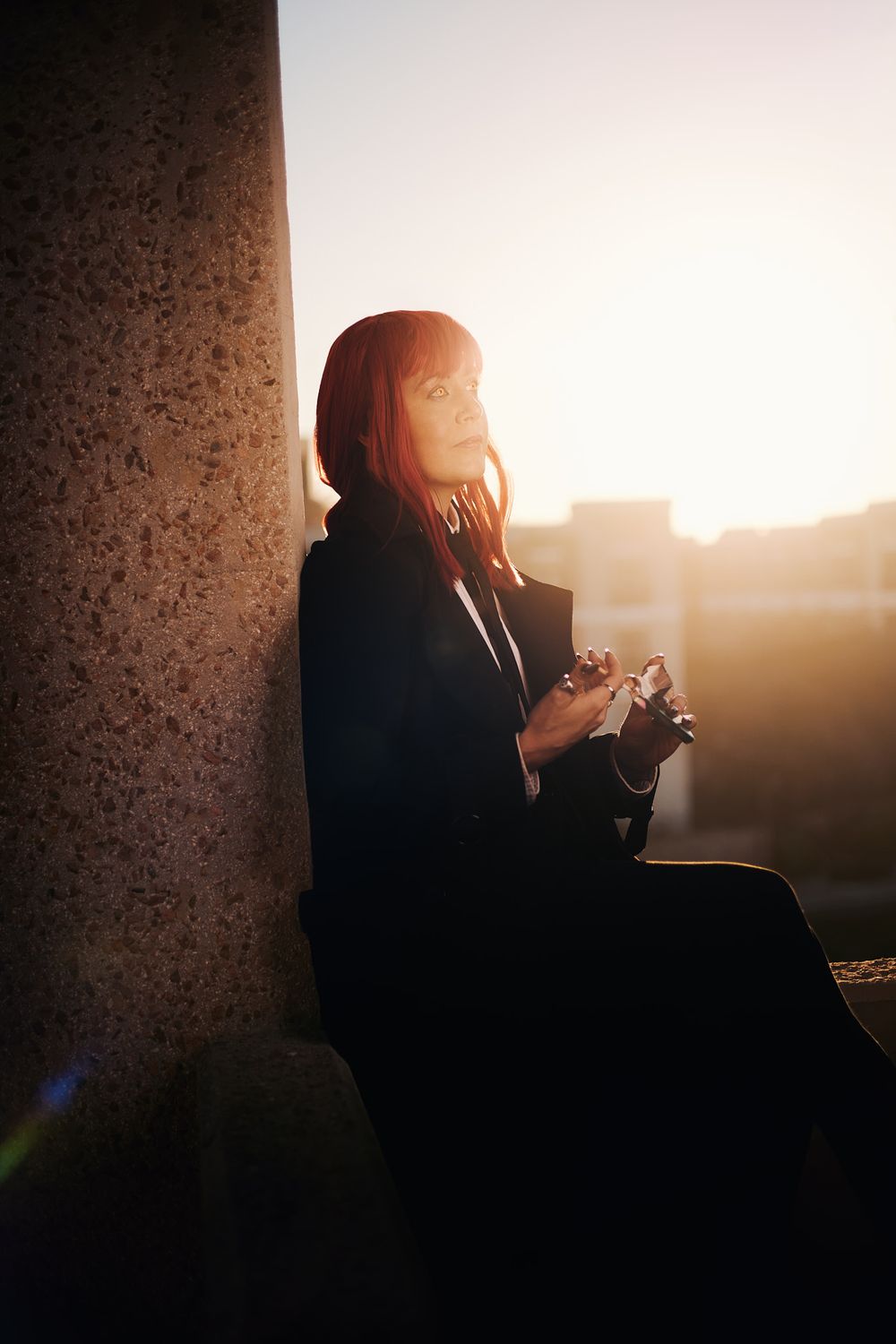 A silhouetted figure sits by a window in dramatic backlighting during sunset creating a moody atmospheric scene.