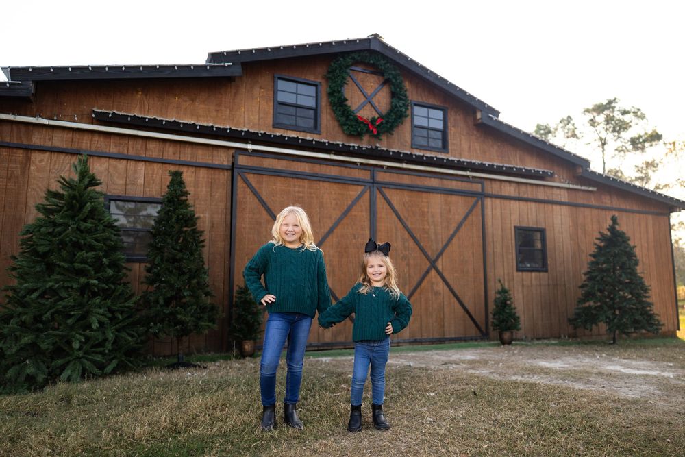 Two people stand in front of rustic barn decorated with Christmas wreath.