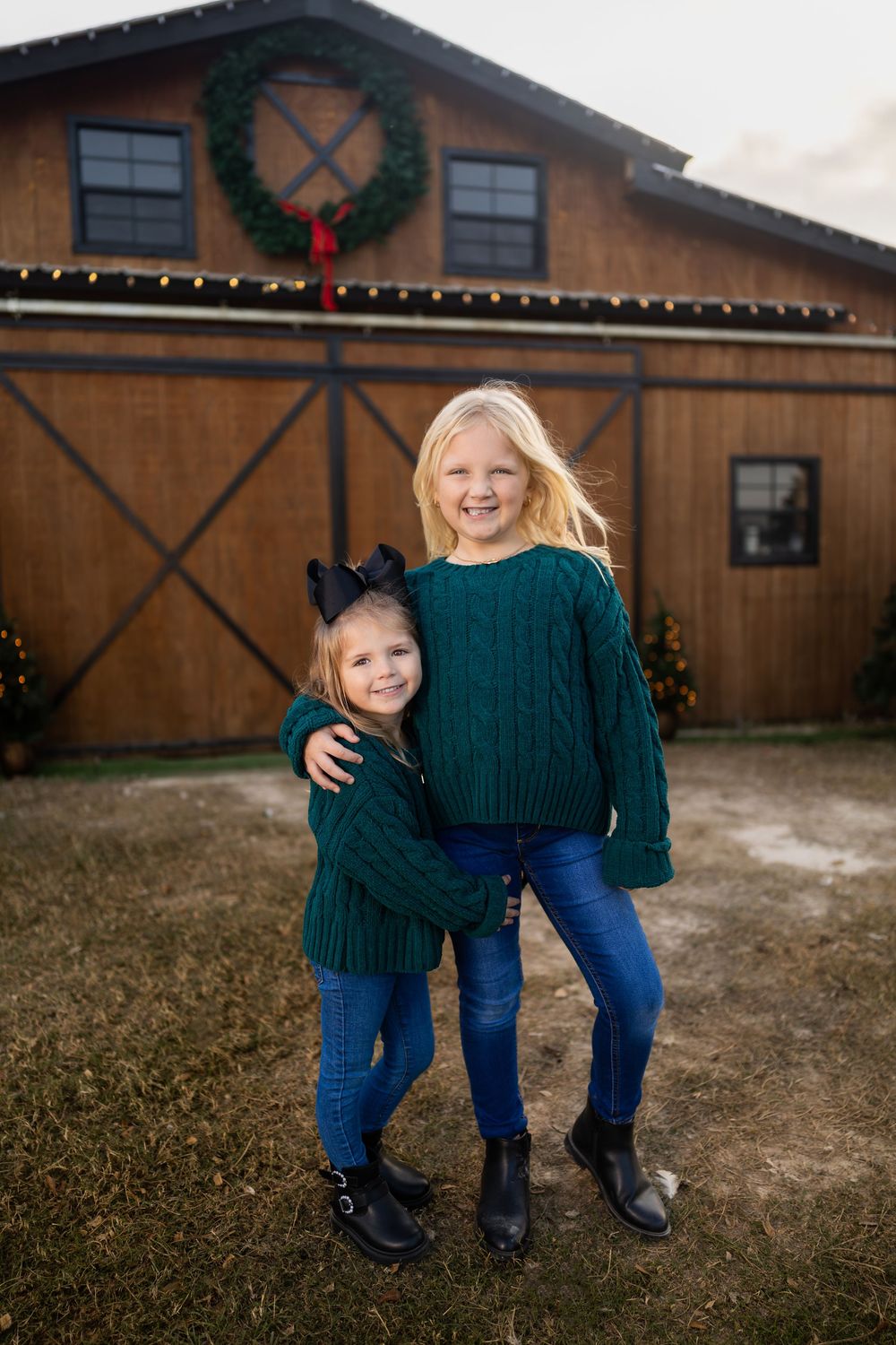 Two children in matching green sweaters pose in front of decorated barn.