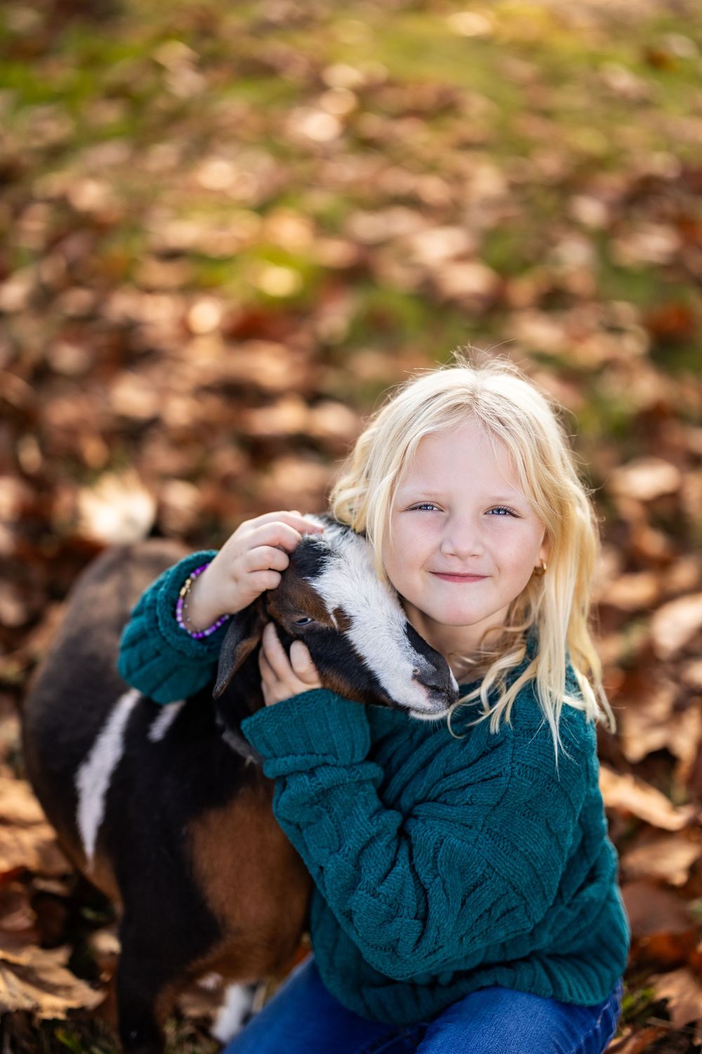 Cuddling with a black and white goat while lying in fallen autumn leaves.