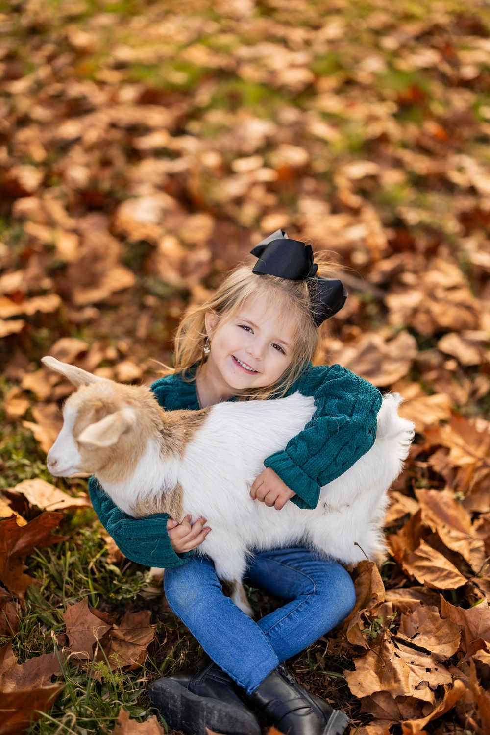 Sharing a tender moment with a white goat while surrounded by autumn foliage.