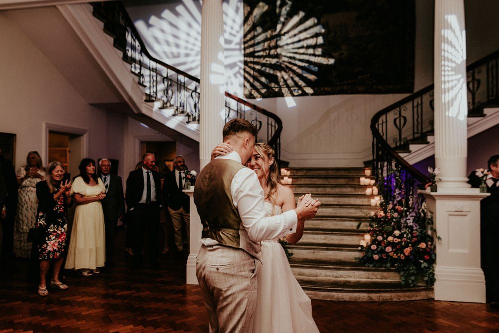 A couple shares their first dance in an elegant ballroom with white columns and romantic lighting. Cornwall wedding photographer