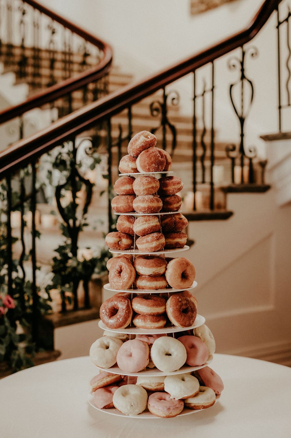 A tiered display of fresh glazed donuts arranged on a white stand against a warm-toned background. Cornwall wedding photographer