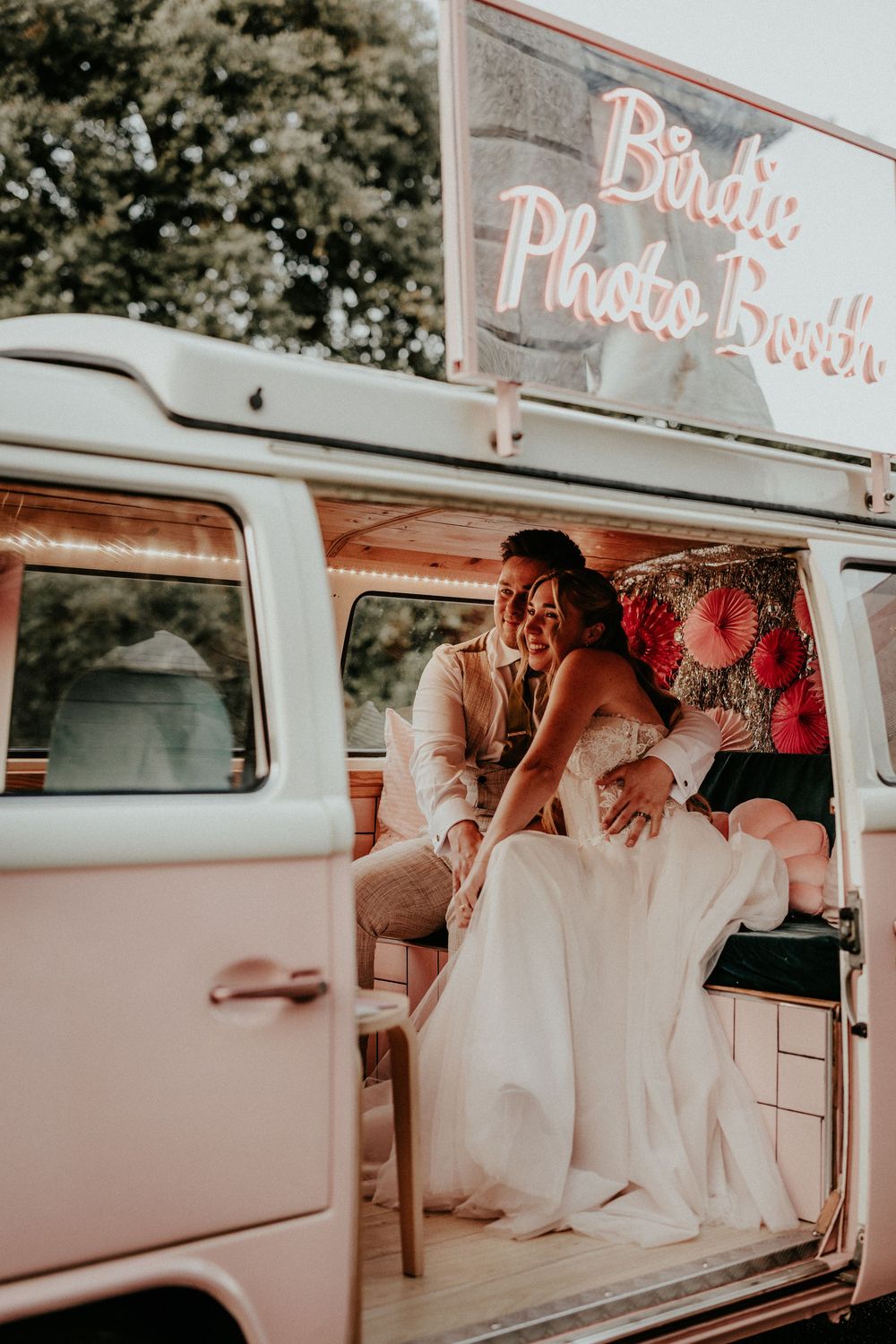 A couple shares a joyful moment inside a vintage Volkswagen van beneath a photo booth sign. Cornwall wedding photographer