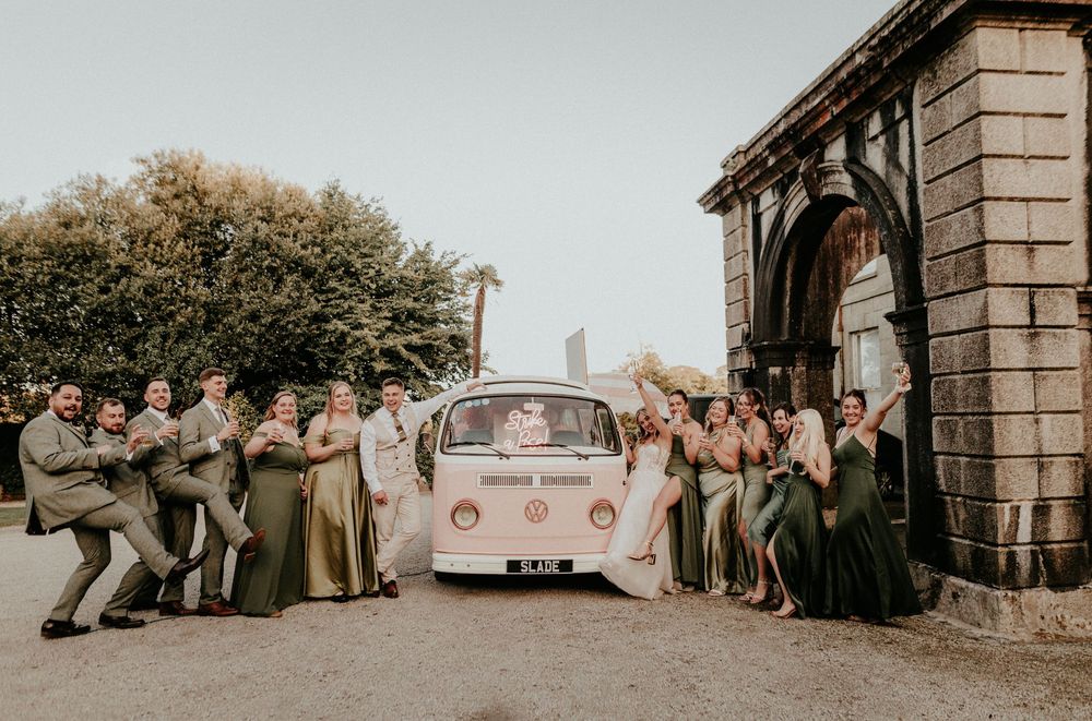 Wedding party poses together in front of stone building entrance in romantic outdoor setting. Cornwall wedding photographer
