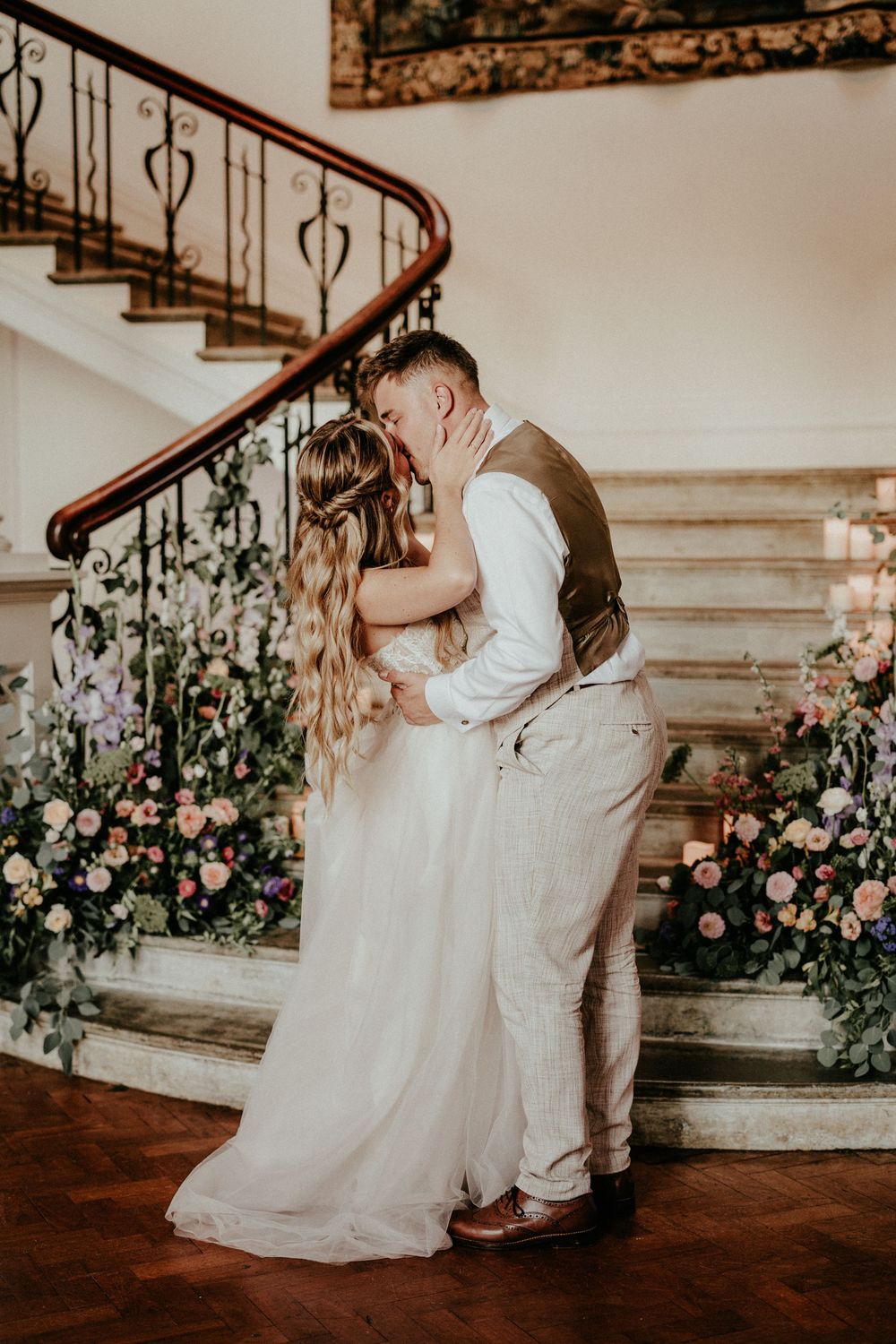 A romantic wedding moment captured on an elegant staircase adorned with floral arrangements. Cornwall wedding photographer