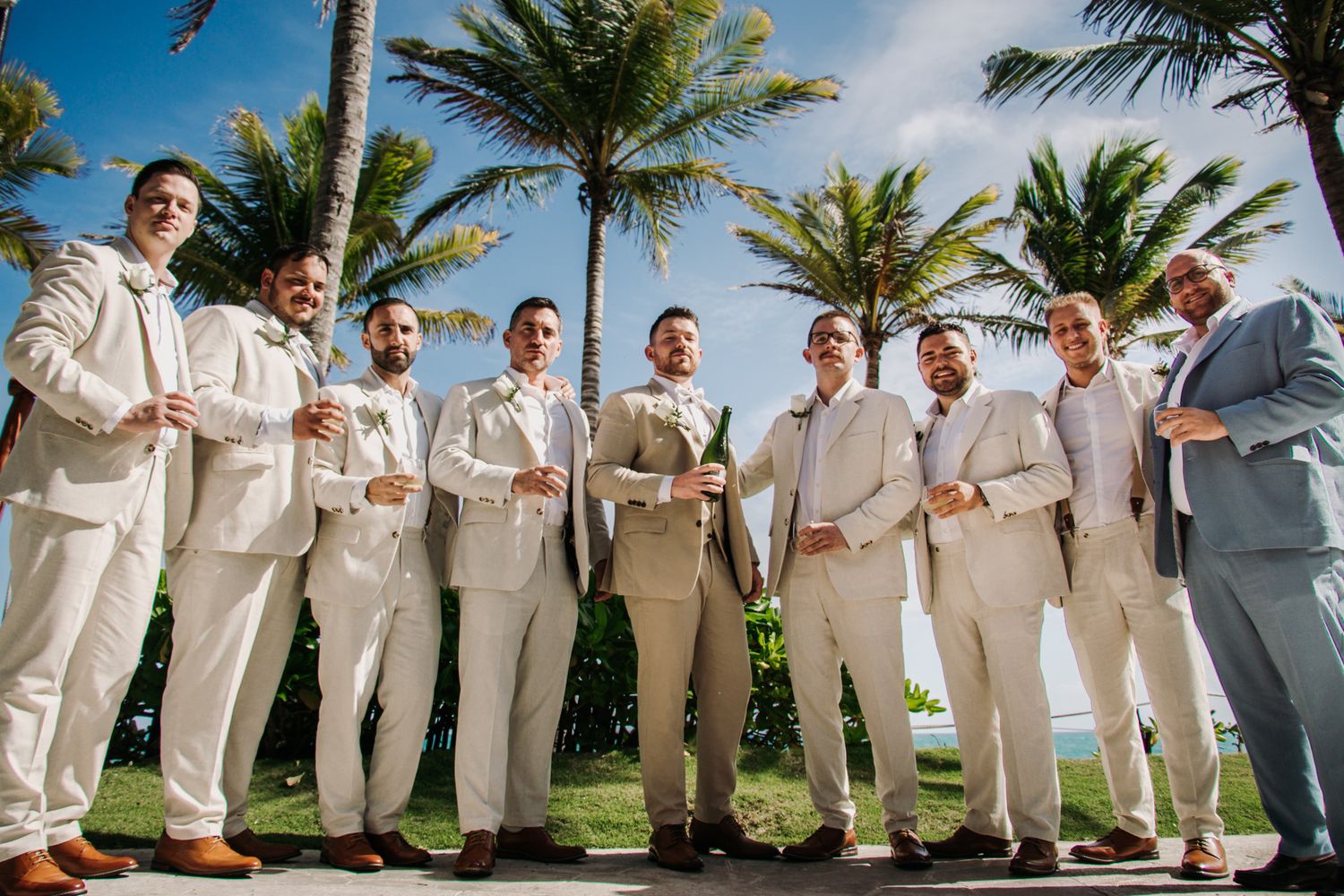 Wedding party members in cream colored suits pose together on a sunny day with palm trees  El Dorado Royale Wedding Photographer