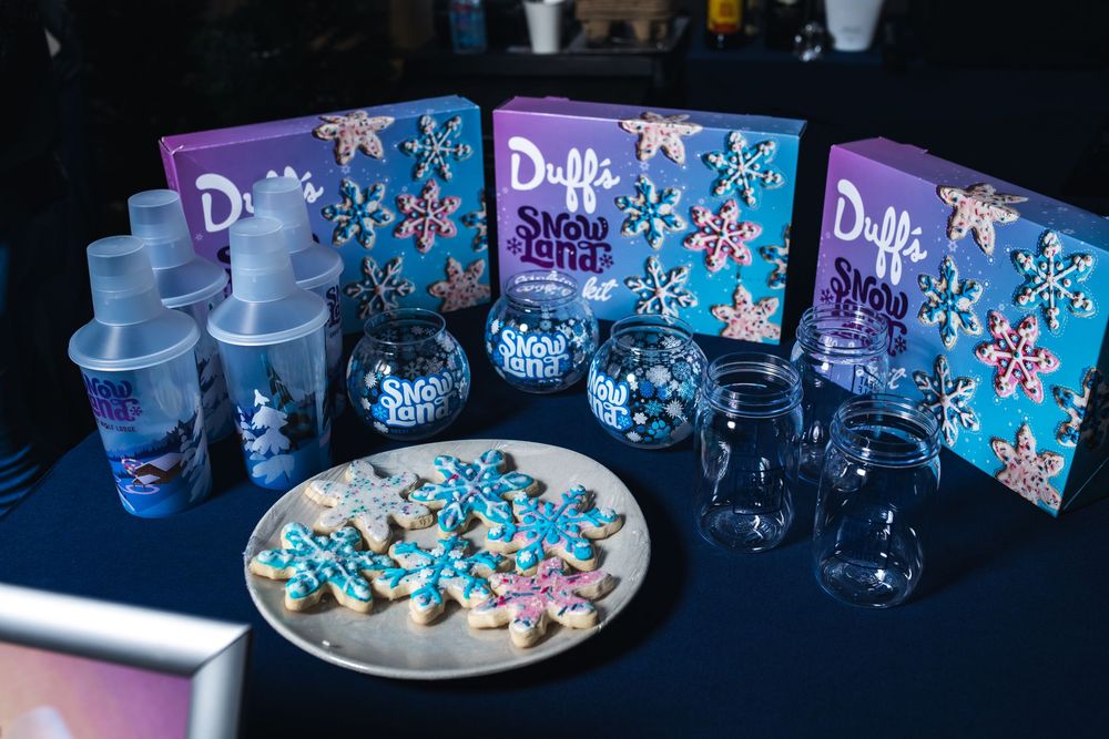 Party setup with blue cookies, drinking glasses, and Duff's Sweet Shop boxes arranged on a dark surface.