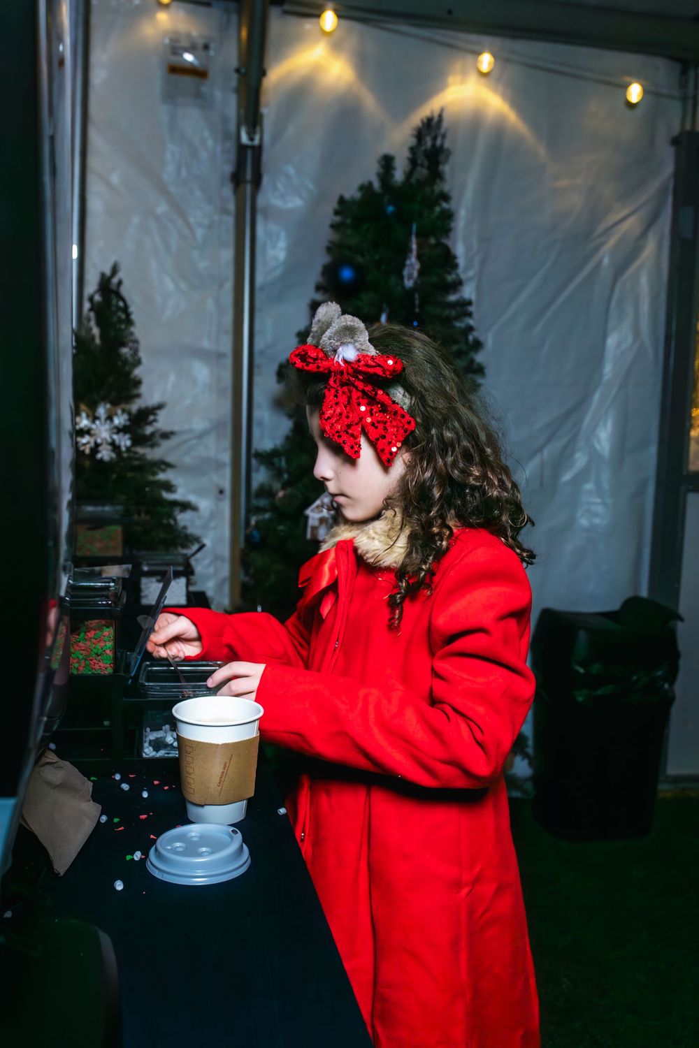Person in a red jacket and polka dot headband dances under string lights at an outdoor evening gathering.
