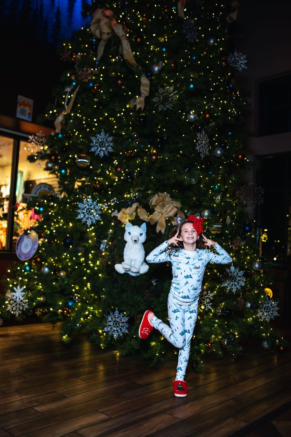 A sequence of playful poses in front of a glowing Christmas tree with snowflake decorations on a wooden floor.