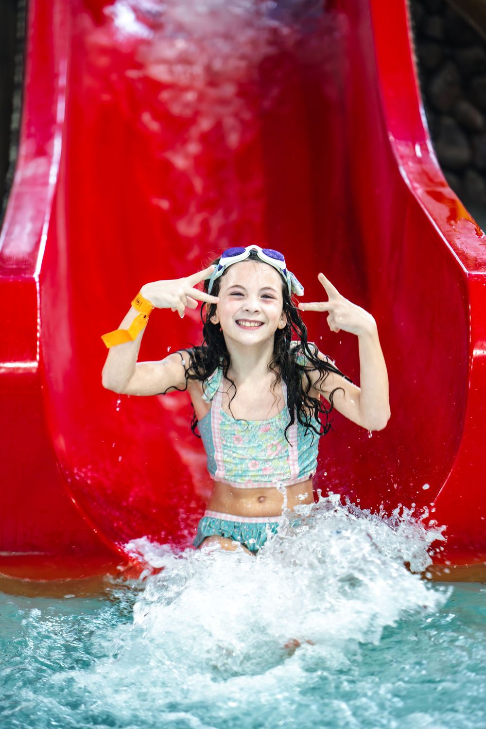 A sequence of four action shots showing someone splashing into the water at the bottom of a bright red water slide.