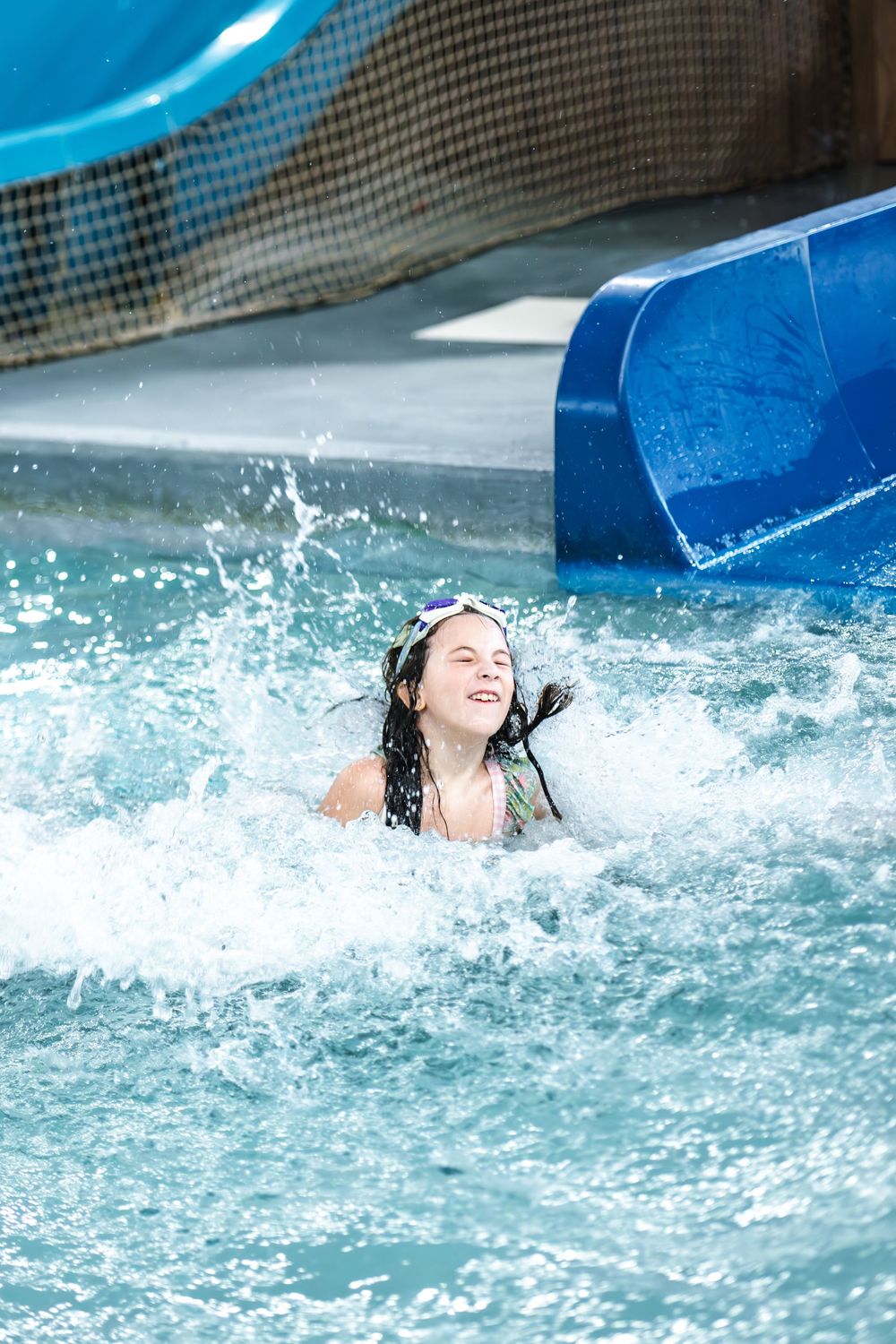 Person splashing in bright blue water at a water park slide landing pool on a sunny day.