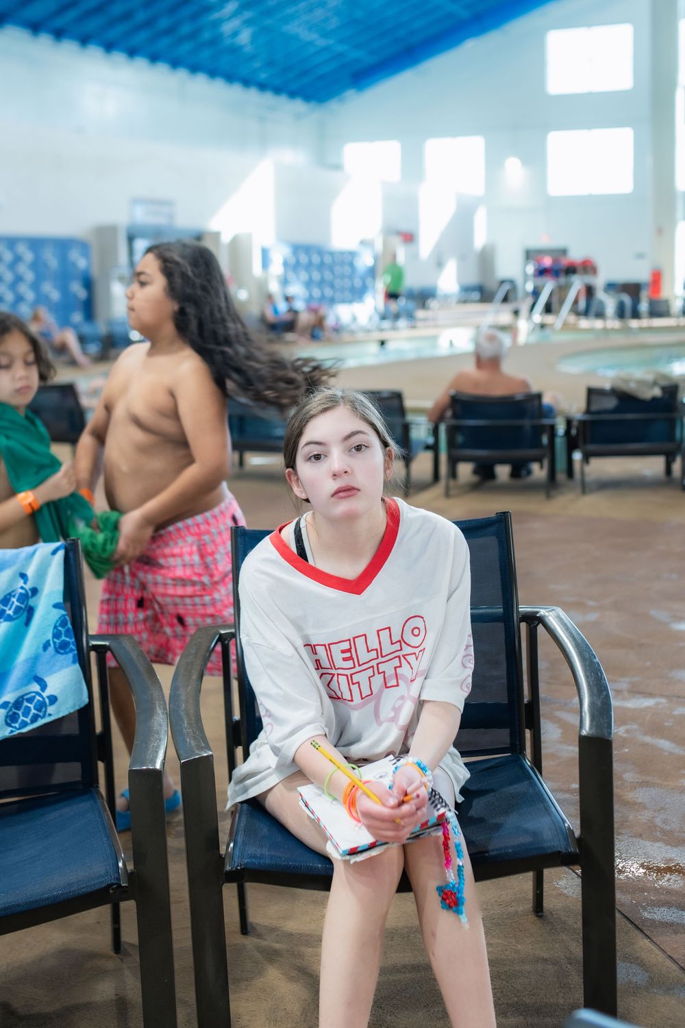 A person in a white and red t-shirt sits on a black chair in what appears to be a community center or cafeteria.
