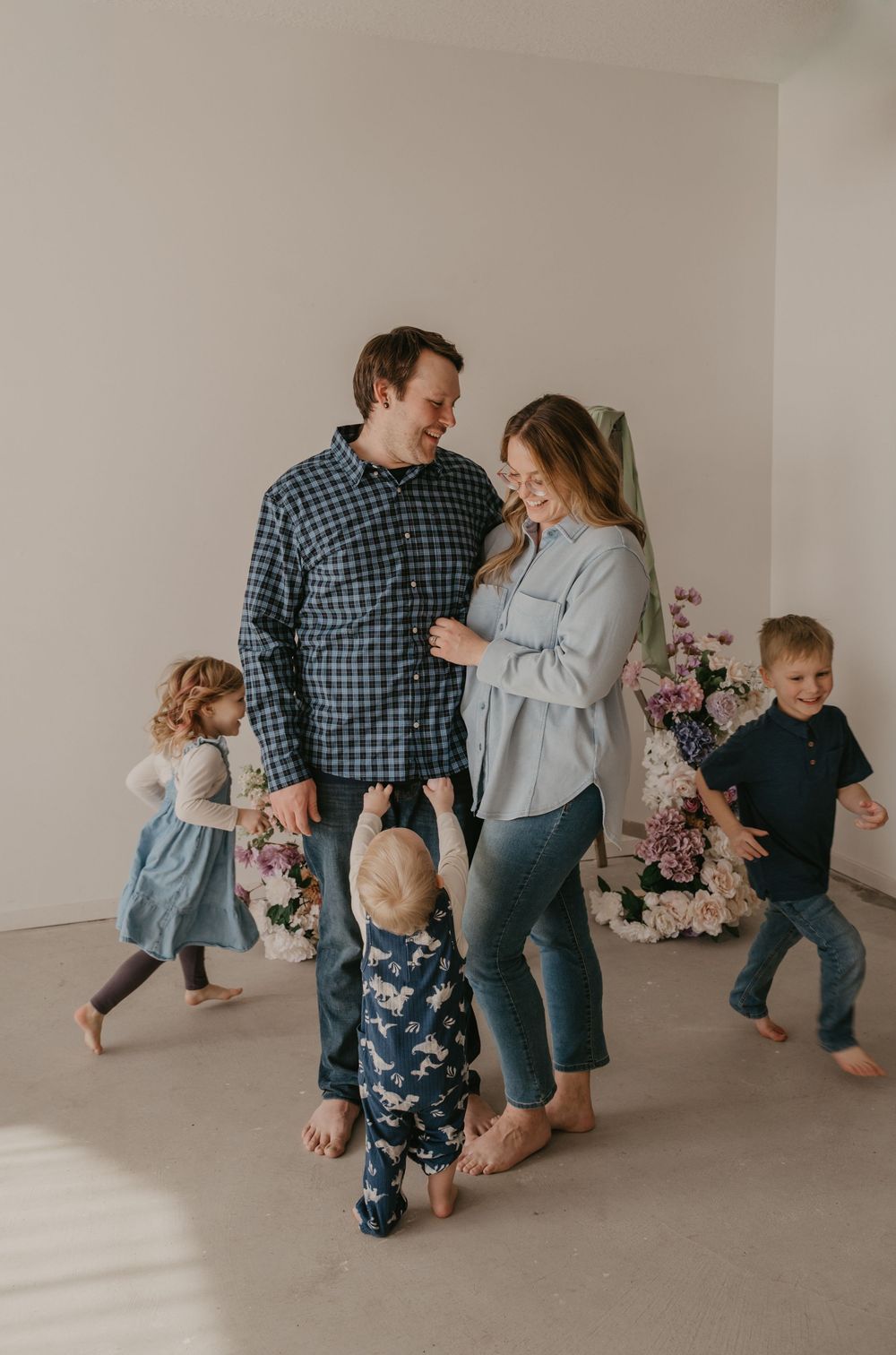 A happy family with three young children dancing and laughing together in a bright studio with floral decor.