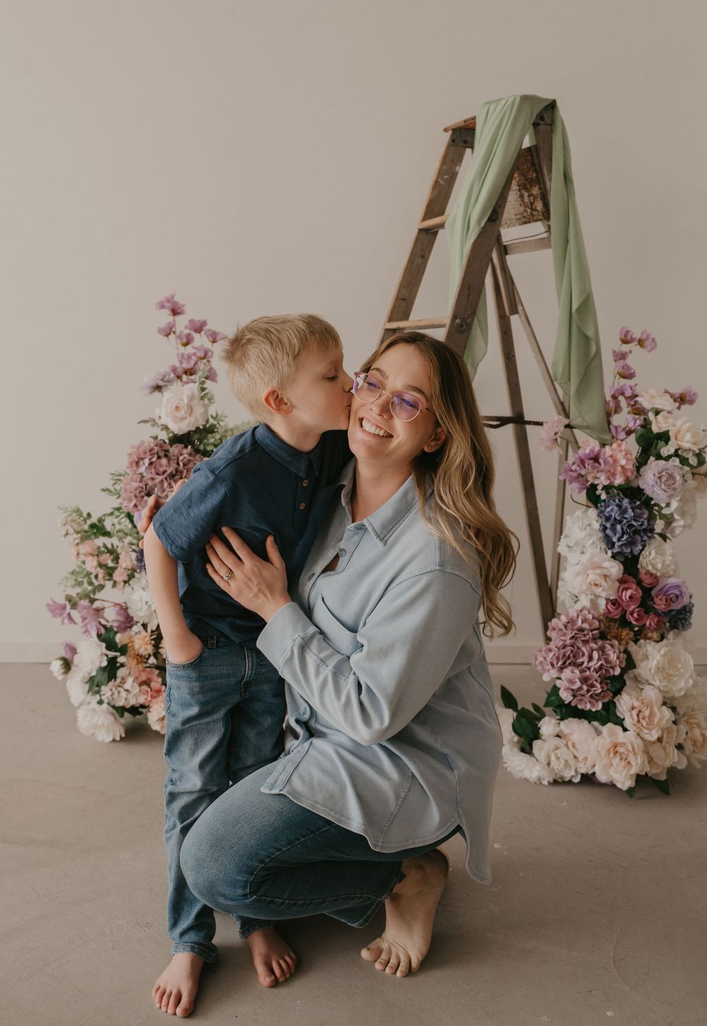 A young boy kisses his smiling mother on the cheek during a floral studio portrait session.