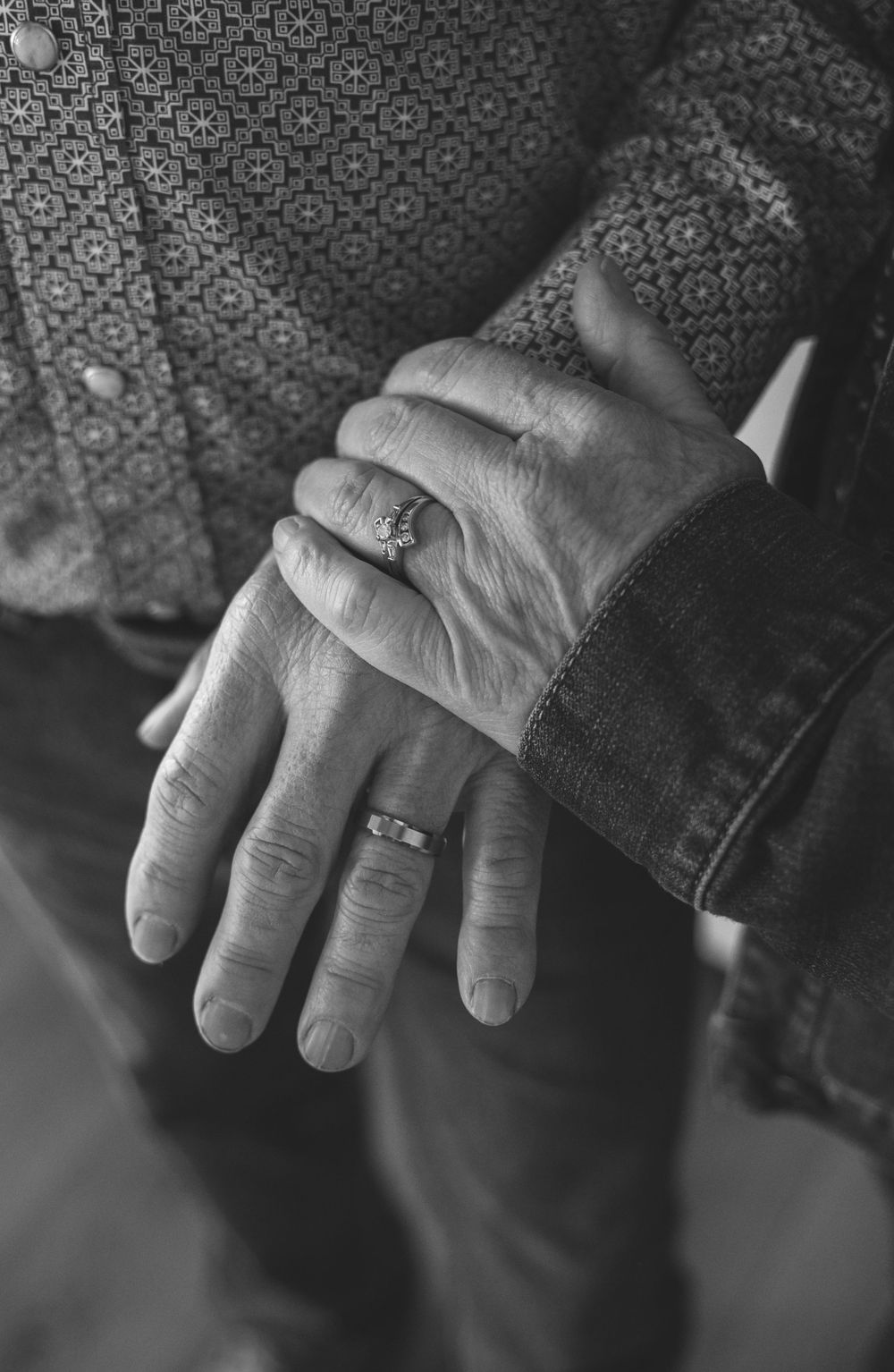 Black and white photo of elderly couple holding hands, wearing wedding rings, symbolizing lasting love and marriage.