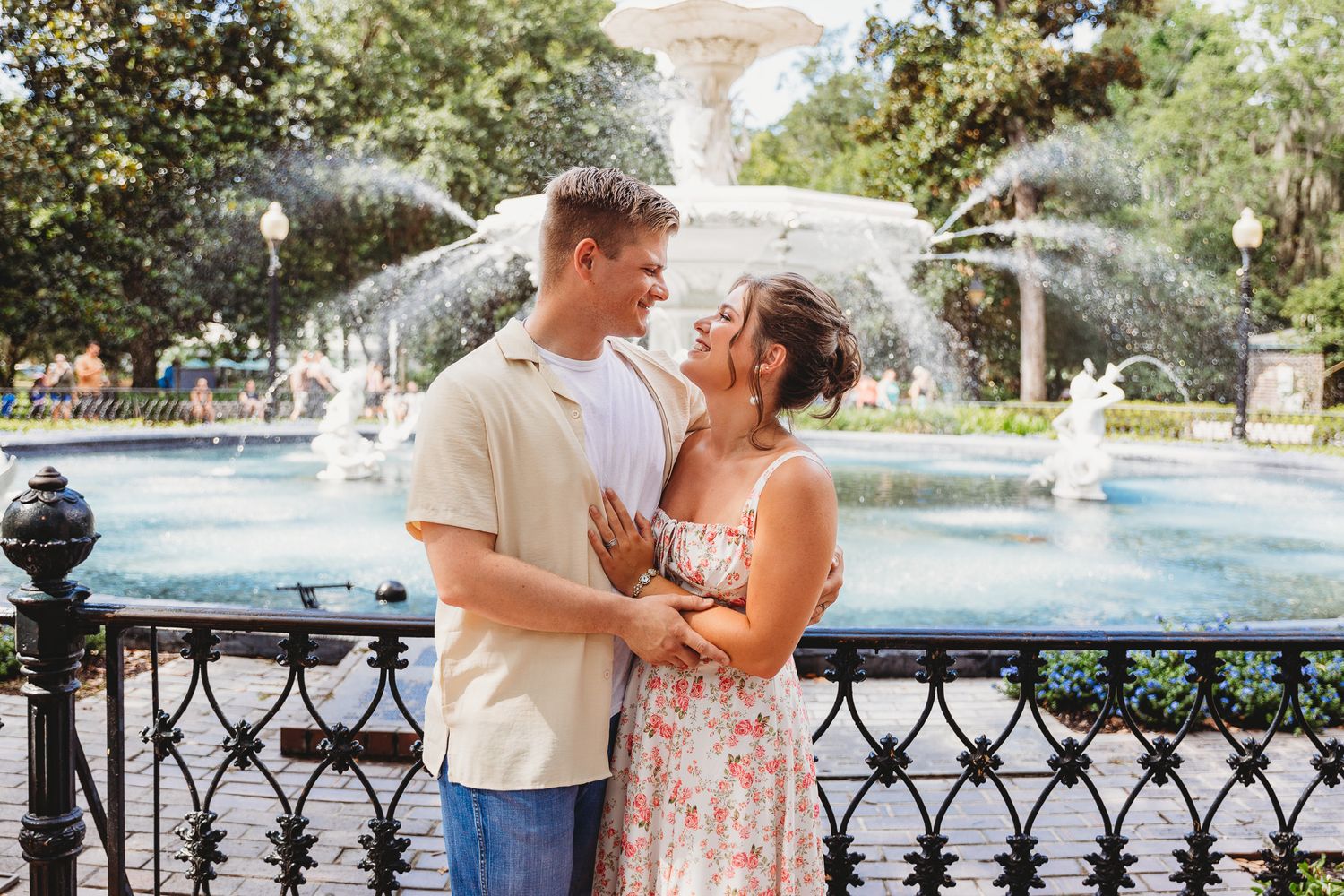 Romantic couple poses by an ornate fountain in a garden setting.