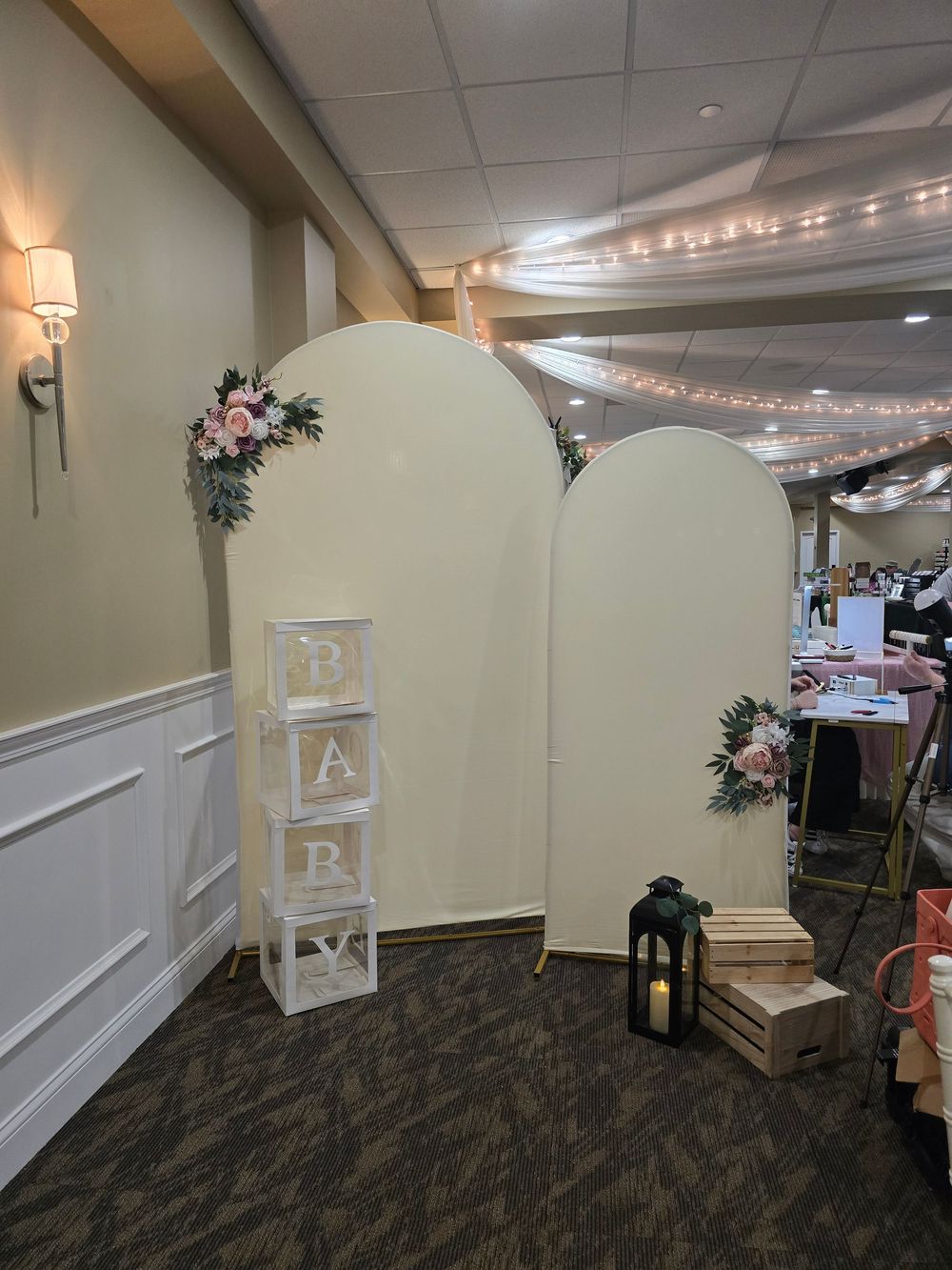 Elegant baby shower venue with cream arch backdrops, floral arrangements, BABY letter blocks, and lantern decor.