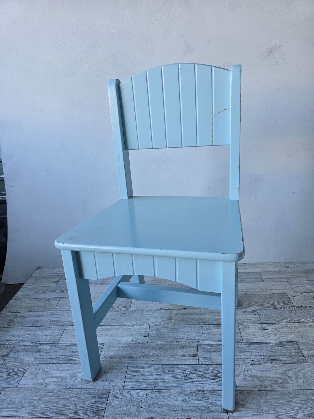 Light blue painted wooden children's chair with slatted back design, displayed on a tiled floor.