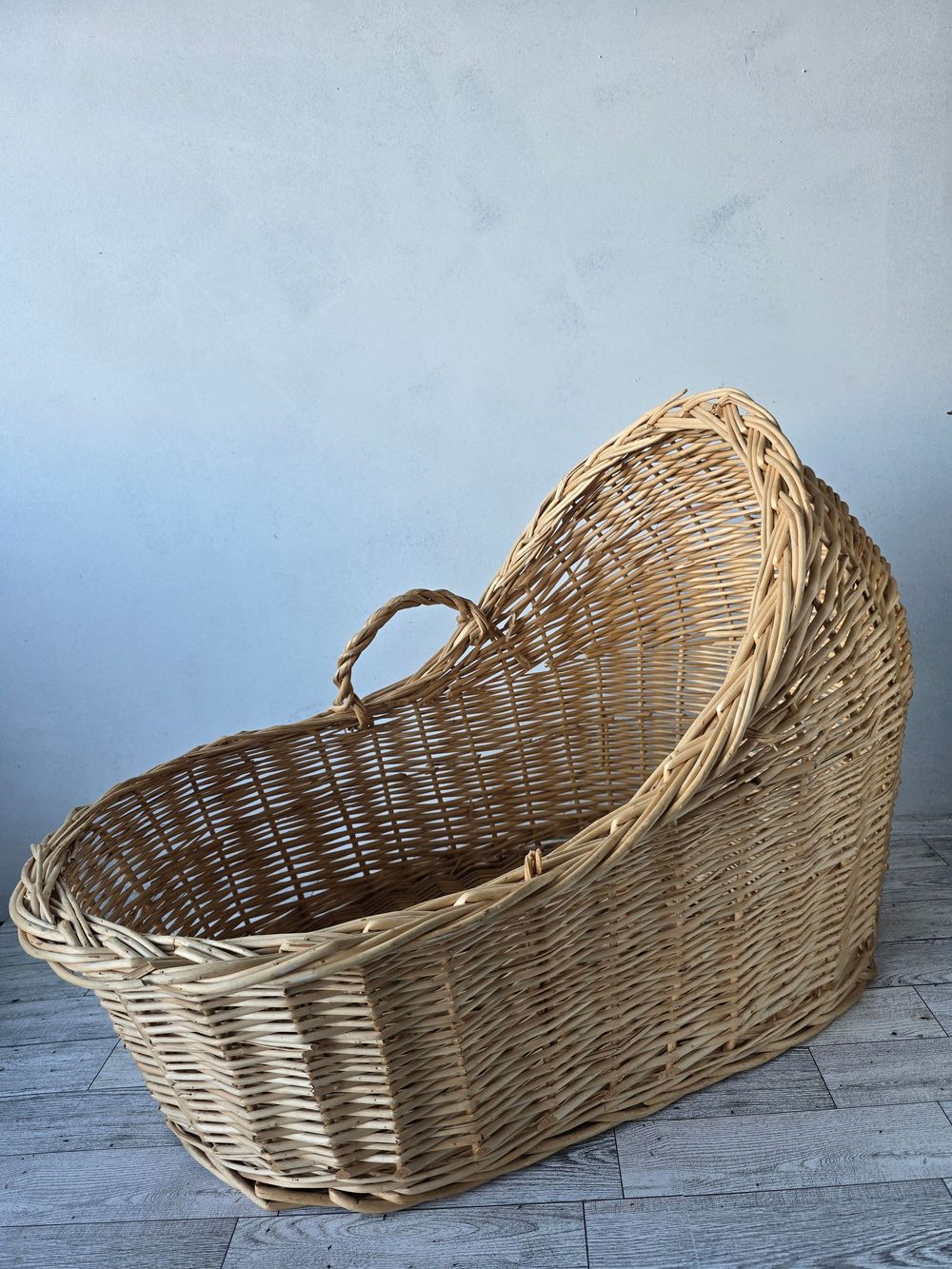 Vintage wicker moses basket with hooded canopy, natural woven rattan baby bassinet on light wood floor.