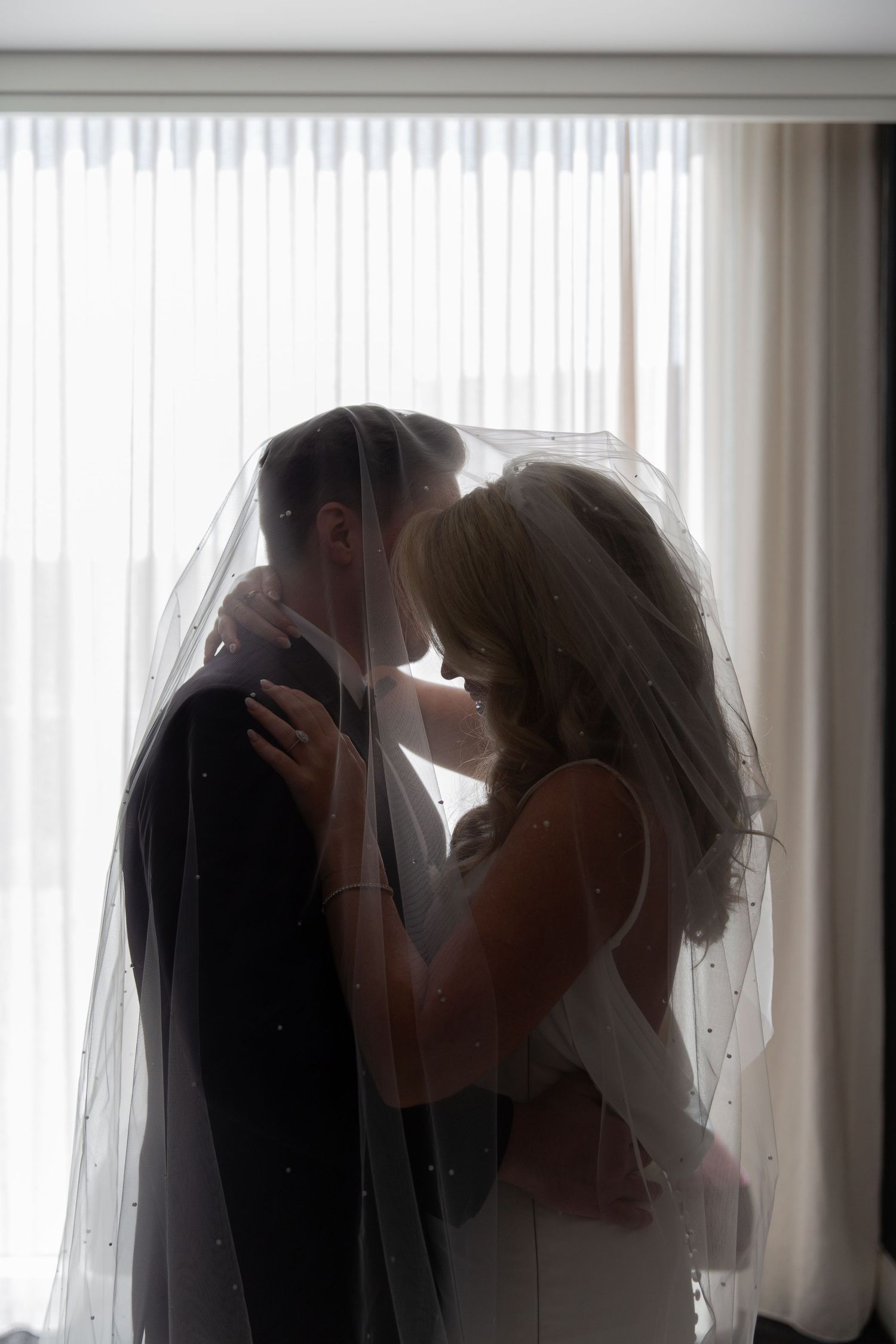 An intimate silhouetted wedding moment captured against bright window light with flowing veil details. NASHVILLE WEDDING PHOTOGRAPHER