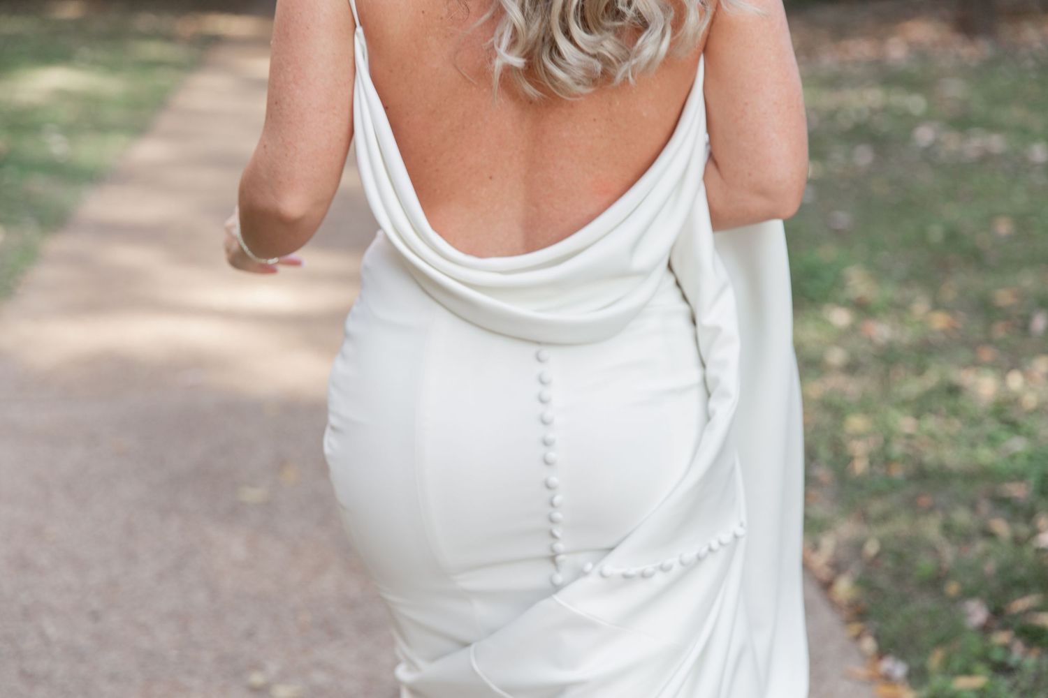 A person wearing a white sleeveless dress walks along a garden path during a sunny day. NASHVILLE WEDDING PHOTOGRAPHER