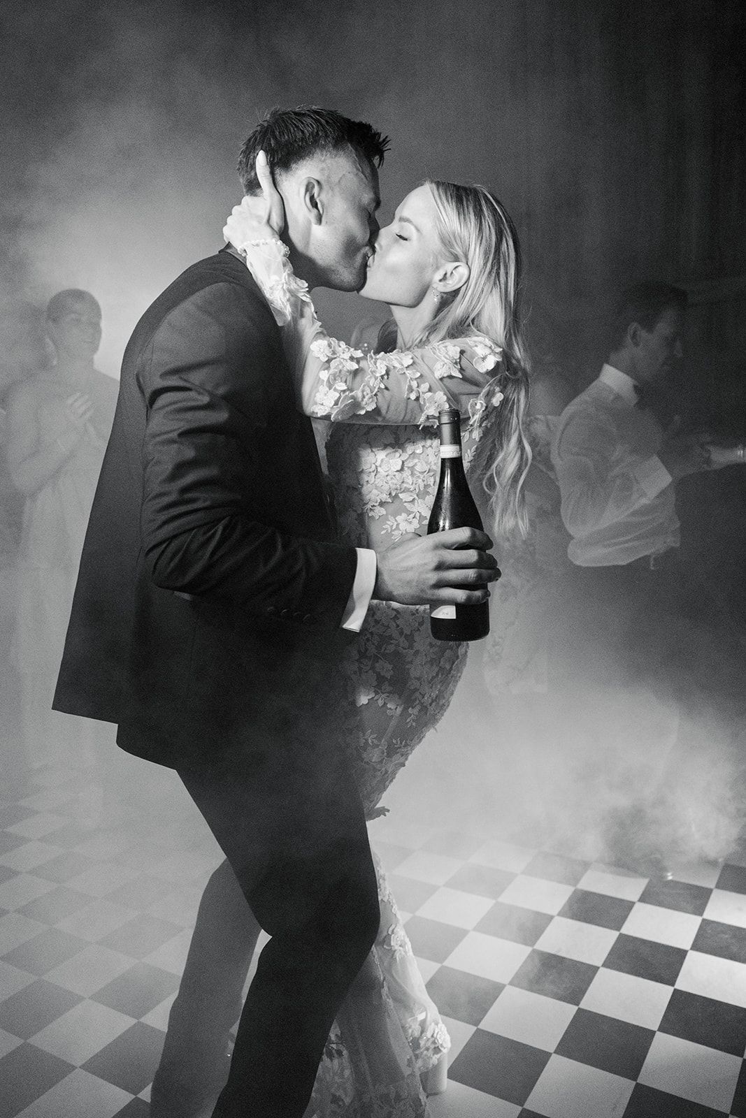 A couple dances romantically on a checkered floor surrounded by atmospheric fog in black and white.