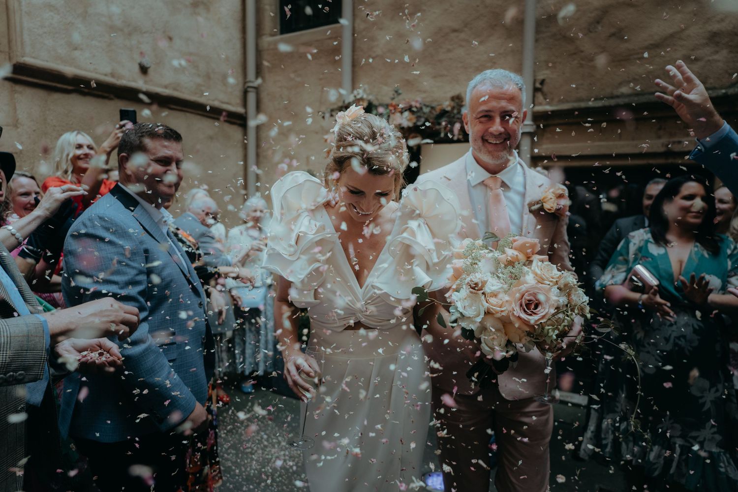 Newlyweds celebrate while walking through shower of confetti with guests.