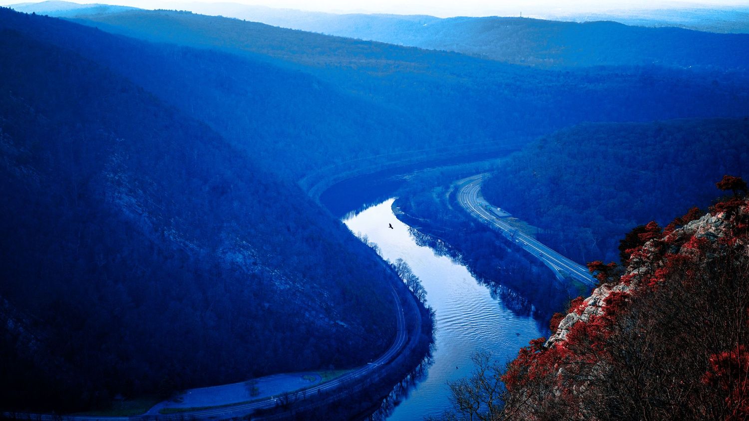 Meandering river cutting through blue-tinted mountain valley landscape.